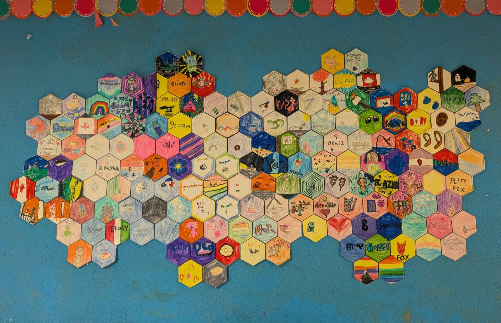 A honeycomb of hexagon tiles, each one decorated by a different student, on a blue board