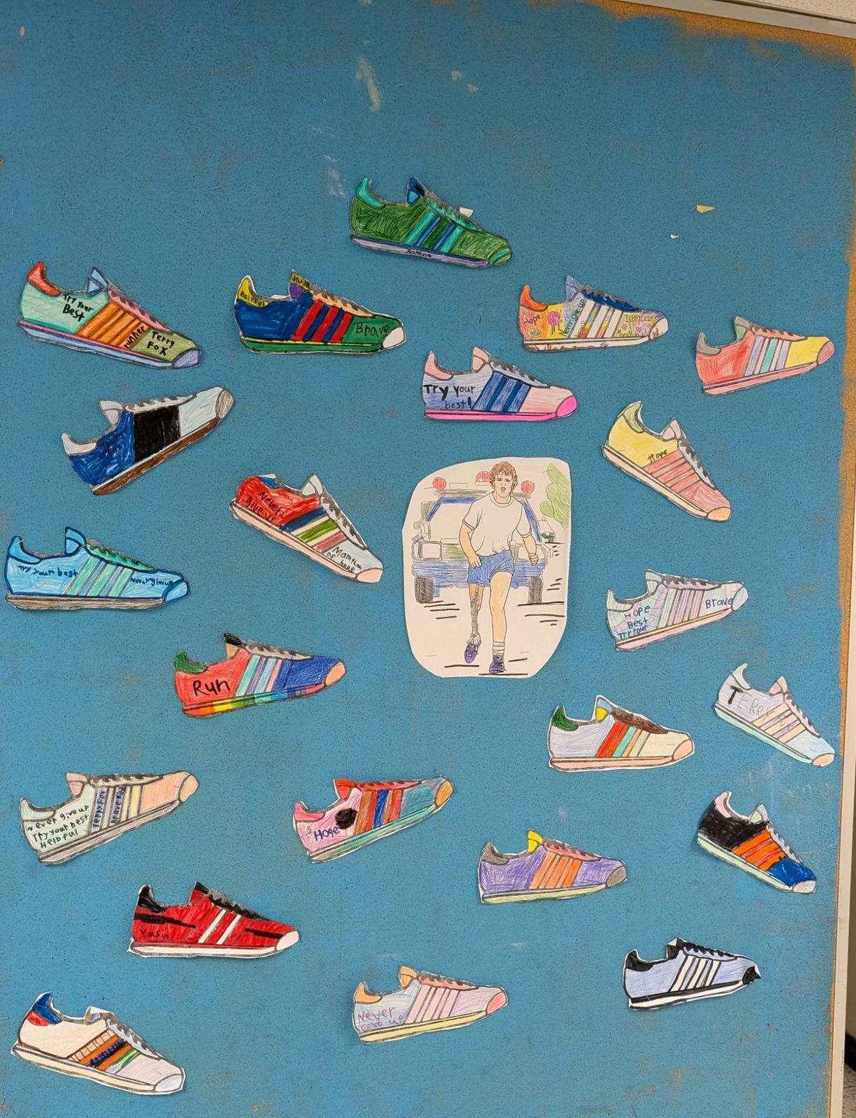 Colourful paper running shoes with messages like Never give up and Try your best around a drawing of Terry Fox